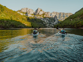 Image showing A group of friends enjoying having fun and kayaking while exploring the calm river, surrounding forest and large natural river canyons