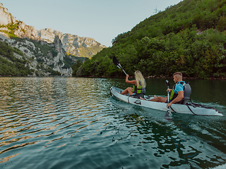 Image showing A young couple enjoying an idyllic kayak ride in the middle of a beautiful river surrounded by forest greenery