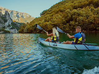 Image showing A young couple enjoying an idyllic kayak ride in the middle of a beautiful river surrounded by forest greenery