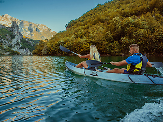 Image showing A young couple enjoying an idyllic kayak ride in the middle of a beautiful river surrounded by forest greenery