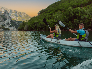 Image showing A young couple enjoying an idyllic kayak ride in the middle of a beautiful river surrounded by forest greenery