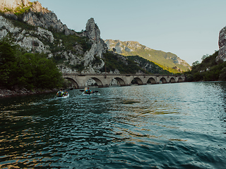 Image showing A group of friends enjoying having fun and kayaking while exploring the calm river, surrounding forest and large natural river canyons