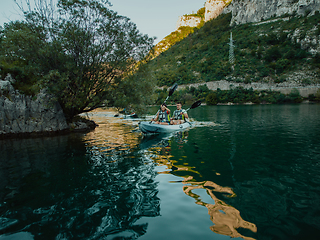 Image showing A group of friends enjoying having fun and kayaking while exploring the calm river, surrounding forest and large natural river canyons