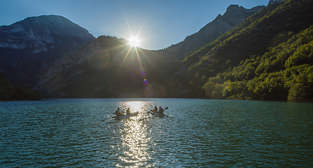 Image showing A group of friends enjoying fun and kayaking exploring the calm river, surrounding forest and large natural river canyons during an idyllic sunset.