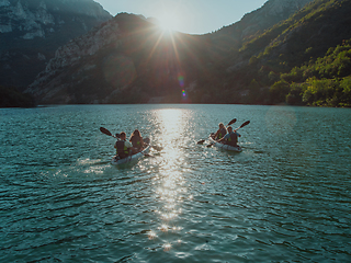 Image showing A group of friends enjoying fun and kayaking exploring the calm river, surrounding forest and large natural river canyons during an idyllic sunset.