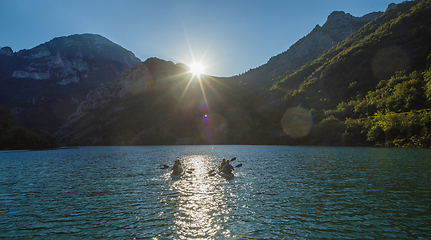 Image showing A group of friends enjoying fun and kayaking exploring the calm river, surrounding forest and large natural river canyons during an idyllic sunset.