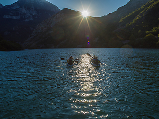 Image showing A group of friends enjoying fun and kayaking exploring the calm river, surrounding forest and large natural river canyons during an idyllic sunset.