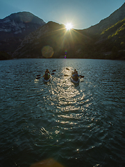 Image showing A group of friends enjoying fun and kayaking exploring the calm river, surrounding forest and large natural river canyons during an idyllic sunset.