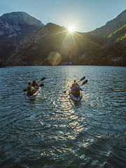 Image showing A group of friends enjoying fun and kayaking exploring the calm river, surrounding forest and large natural river canyons during an idyllic sunset.