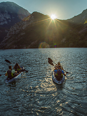 Image showing A group of friends enjoying fun and kayaking exploring the calm river, surrounding forest and large natural river canyons during an idyllic sunset.