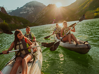 Image showing A group of friends enjoying fun and kayaking exploring the calm river, surrounding forest and large natural river canyons during an idyllic sunset.