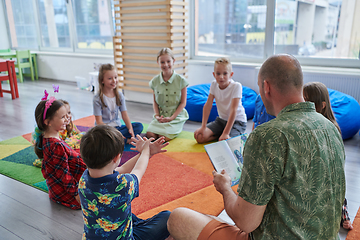 Image showing Reading time in an elementary school or kindergarten, a teacher reading a book to children in an elementary school or kindergarten. The concept of pre-school education. Selective focus