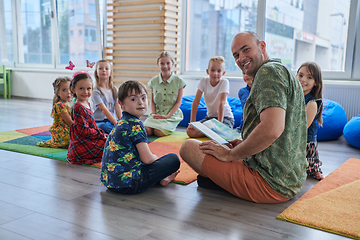 Image showing Reading time in an elementary school or kindergarten, a teacher reading a book to children in an elementary school or kindergarten. The concept of pre-school education. Selective focus