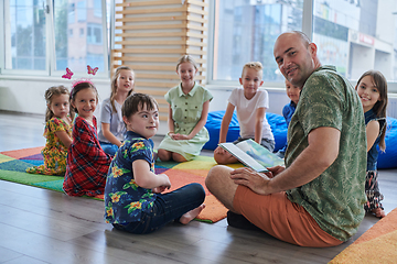 Image showing Reading time in an elementary school or kindergarten, a teacher reading a book to children in an elementary school or kindergarten. The concept of pre-school education. Selective focus