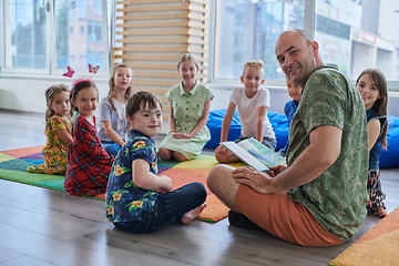 Image showing Reading time in an elementary school or kindergarten, a teacher reading a book to children in an elementary school or kindergarten. The concept of pre-school education. Selective focus