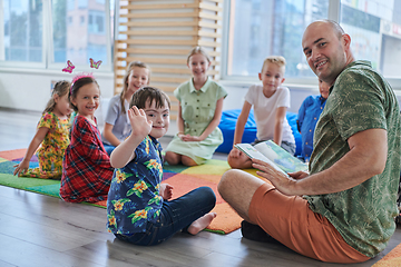 Image showing Reading time in an elementary school or kindergarten, a teacher reading a book to children in an elementary school or kindergarten. The concept of pre-school education. Selective focus