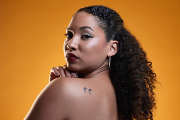 Image showing Beauty, portrait and a woman with a tattoo in studio for cosmetics, makeup and dermatology. Closeup of a young female model on an orange background in studio with body art, confidence and skin glow