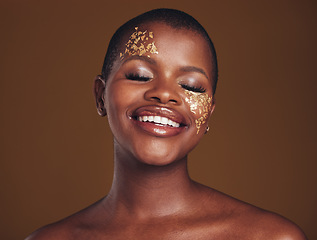 Image showing Gold, glitter and black woman smile from beauty with makeup and studio with sparkle cosmetics. Brown background, relax and female model with golden paint for skin glow and creative facial shine