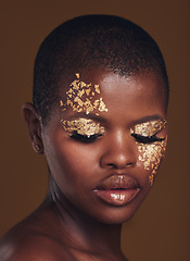 Image showing Gold flakes, beauty and black woman with face closeup with makeup and cosmetics in studio. Brown background, African female model and glitter with golden shine and glow from facial paint sparkle