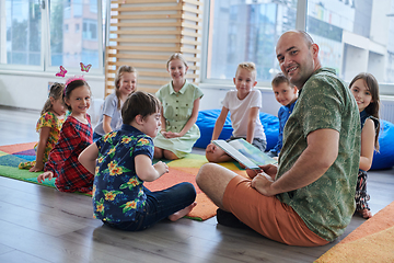 Image showing Reading time in an elementary school or kindergarten, a teacher reading a book to children in an elementary school or kindergarten. The concept of pre-school education. Selective focus