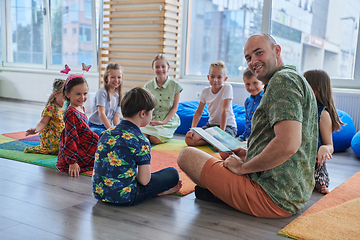 Image showing Reading time in an elementary school or kindergarten, a teacher reading a book to children in an elementary school or kindergarten. The concept of pre-school education. Selective focus