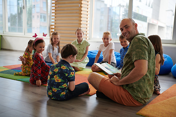 Image showing Reading time in an elementary school or kindergarten, a teacher reading a book to children in an elementary school or kindergarten. The concept of pre-school education. Selective focus