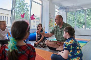 Image showing Reading time in an elementary school or kindergarten, a teacher reading a book to children in an elementary school or kindergarten. The concept of pre-school education. Selective focus