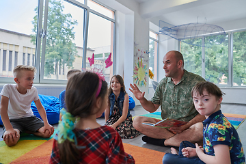 Image showing Reading time in an elementary school or kindergarten, a teacher reading a book to children in an elementary school or kindergarten. The concept of pre-school education. Selective focus