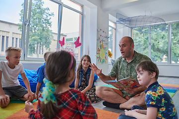 Image showing Reading time in an elementary school or kindergarten, a teacher reading a book to children in an elementary school or kindergarten. The concept of pre-school education. Selective focus