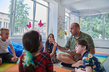 Image showing Reading time in an elementary school or kindergarten, a teacher reading a book to children in an elementary school or kindergarten. The concept of pre-school education. Selective focus