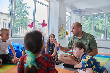 Image showing Reading time in an elementary school or kindergarten, a teacher reading a book to children in an elementary school or kindergarten. The concept of pre-school education. Selective focus