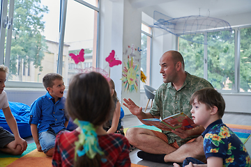 Image showing Reading time in an elementary school or kindergarten, a teacher reading a book to children in an elementary school or kindergarten. The concept of pre-school education. Selective focus