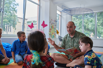 Image showing Reading time in an elementary school or kindergarten, a teacher reading a book to children in an elementary school or kindergarten. The concept of pre-school education. Selective focus