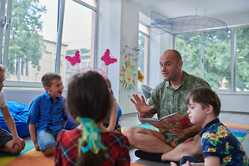 Image showing Reading time in an elementary school or kindergarten, a teacher reading a book to children in an elementary school or kindergarten. The concept of pre-school education. Selective focus