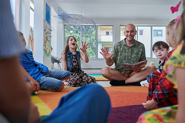 Image showing Reading time in an elementary school or kindergarten, a teacher reading a book to children in an elementary school or kindergarten. The concept of pre-school education. Selective focus