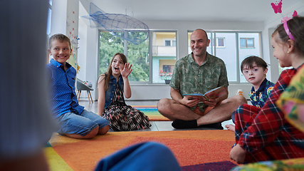 Image showing Reading time in an elementary school or kindergarten, a teacher reading a book to children in an elementary school or kindergarten. The concept of pre-school education. Selective focus