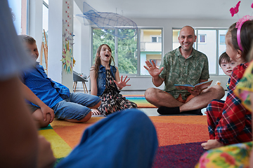 Image showing Reading time in an elementary school or kindergarten, a teacher reading a book to children in an elementary school or kindergarten. The concept of pre-school education. Selective focus