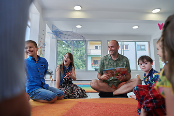 Image showing Reading time in an elementary school or kindergarten, a teacher reading a book to children in an elementary school or kindergarten. The concept of pre-school education. Selective focus