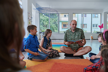 Image showing Reading time in an elementary school or kindergarten, a teacher reading a book to children in an elementary school or kindergarten. The concept of pre-school education. Selective focus