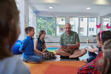 Image showing Reading time in an elementary school or kindergarten, a teacher reading a book to children in an elementary school or kindergarten. The concept of pre-school education. Selective focus