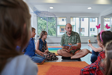 Image showing Reading time in an elementary school or kindergarten, a teacher reading a book to children in an elementary school or kindergarten. The concept of pre-school education. Selective focus