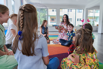 Image showing Reading time in an elementary school or kindergarten, a teacher reading a book to children in an elementary school or kindergarten. The concept of pre-school education. Selective focus