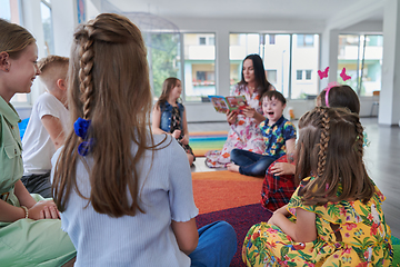 Image showing Reading time in an elementary school or kindergarten, a teacher reading a book to children in an elementary school or kindergarten. The concept of pre-school education. Selective focus