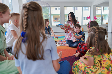 Image showing Reading time in an elementary school or kindergarten, a teacher reading a book to children in an elementary school or kindergarten. The concept of pre-school education. Selective focus