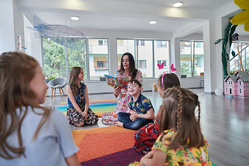 Image showing Reading time in an elementary school or kindergarten, a teacher reading a book to children in an elementary school or kindergarten. The concept of pre-school education. Selective focus