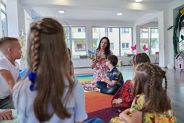 Image showing Reading time in an elementary school or kindergarten, a teacher reading a book to children in an elementary school or kindergarten. The concept of pre-school education. Selective focus