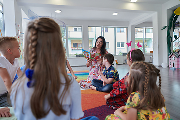 Image showing Reading time in an elementary school or kindergarten, a teacher reading a book to children in an elementary school or kindergarten. The concept of pre-school education. Selective focus