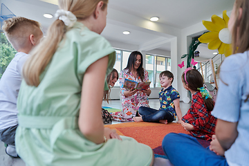 Image showing Reading time in an elementary school or kindergarten, a teacher reading a book to children in an elementary school or kindergarten. The concept of pre-school education. Selective focus