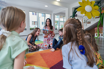 Image showing Reading time in an elementary school or kindergarten, a teacher reading a book to children in an elementary school or kindergarten. The concept of pre-school education. Selective focus