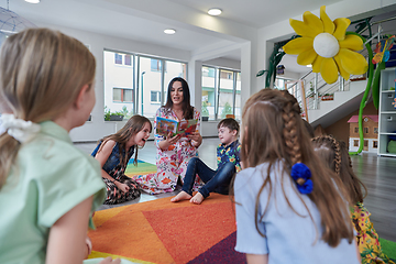 Image showing Reading time in an elementary school or kindergarten, a teacher reading a book to children in an elementary school or kindergarten. The concept of pre-school education. Selective focus